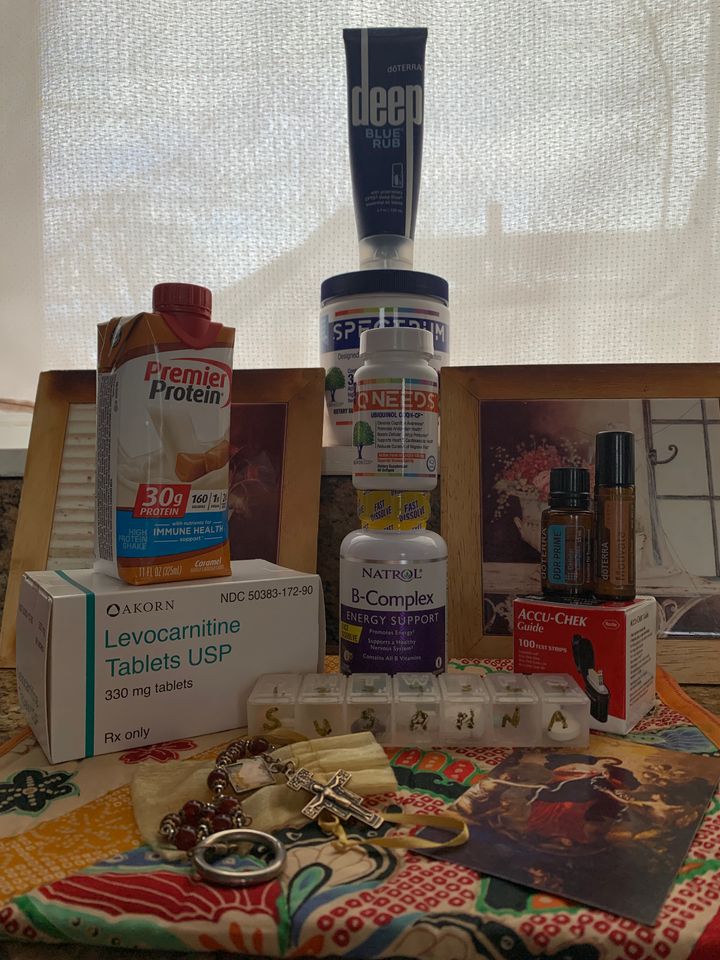 Artfully arranged objects including Protein drink, Levocarnitine Tablets, Rosary, pill container, Q Needs, Spectrum Needs